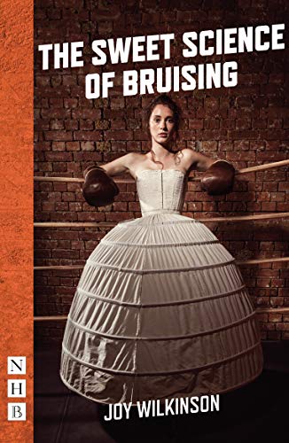 A woman in a white Victorian dress and boxing gloves stands in a ring.