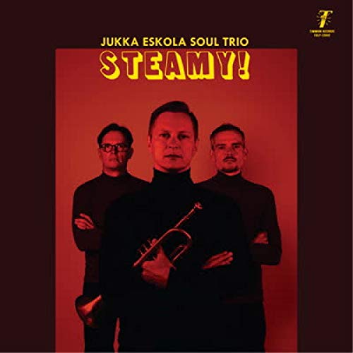 Three men in black turtlenecks stand against a red background, one holding a trumpet.