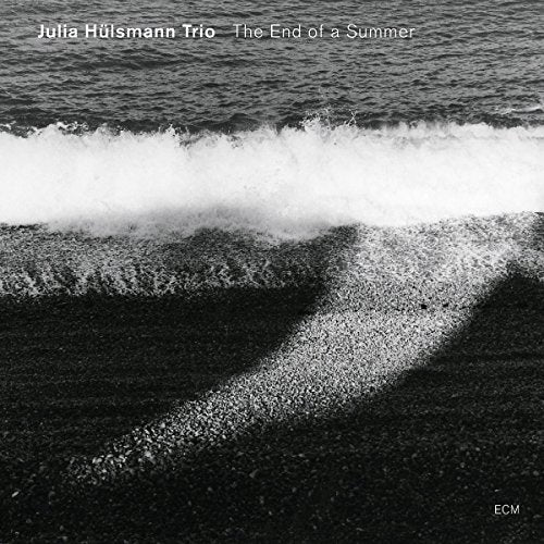 A black-and-white photo of a wave on a sandy beach, album cover.