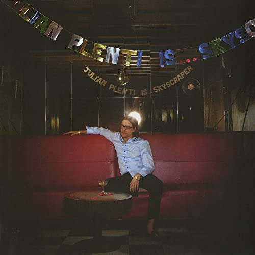 Album cover featuring a man on a red couch with colorful garland.