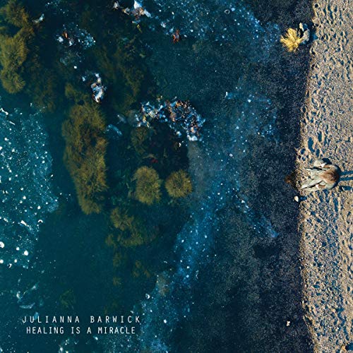 Aerial view of blue water, sand, and scattered debris; album cover.