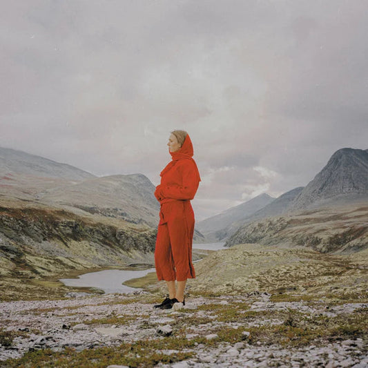 Woman in red coat stands in a mountainous, snowy landscape.