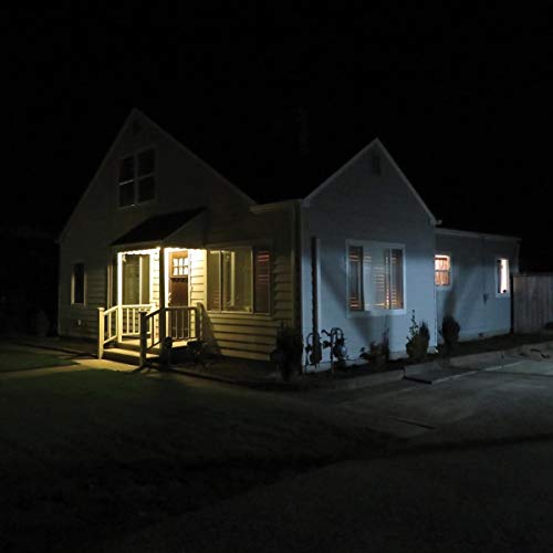 The image depicts a house at night. The alt text is: "White house with porch and lit windows at night."