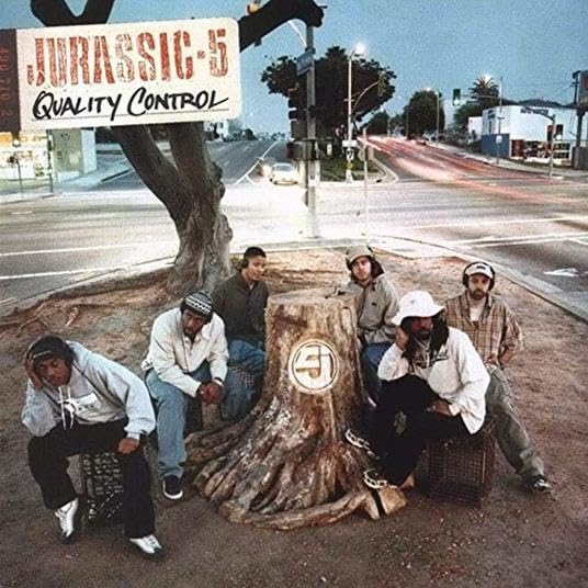 Jurassic-5 album cover: group seated around a tree stump in a city.