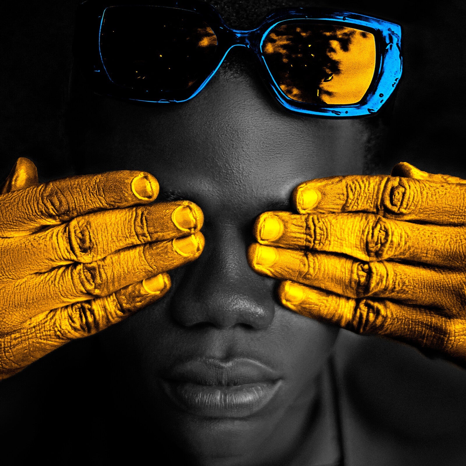 Person with golden hands covering eyes, reflected in sunglasses.