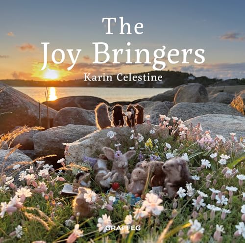 Small felt animal figures gather among wildflowers by a rocky shore at sunset.