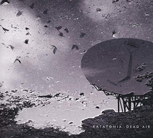 A satellite dish on a rocky surface with birds flying in a dark sky.