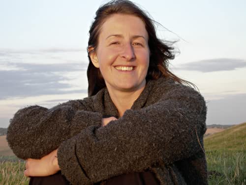 Smiling woman with brown hair outdoors, wearing a gray sweater.