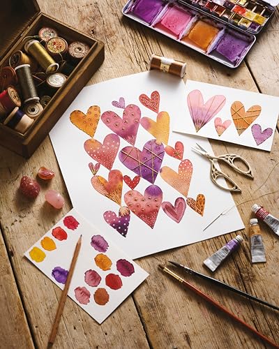 Art supplies, watercolor hearts, and embroidery thread arranged on a rustic wooden table.