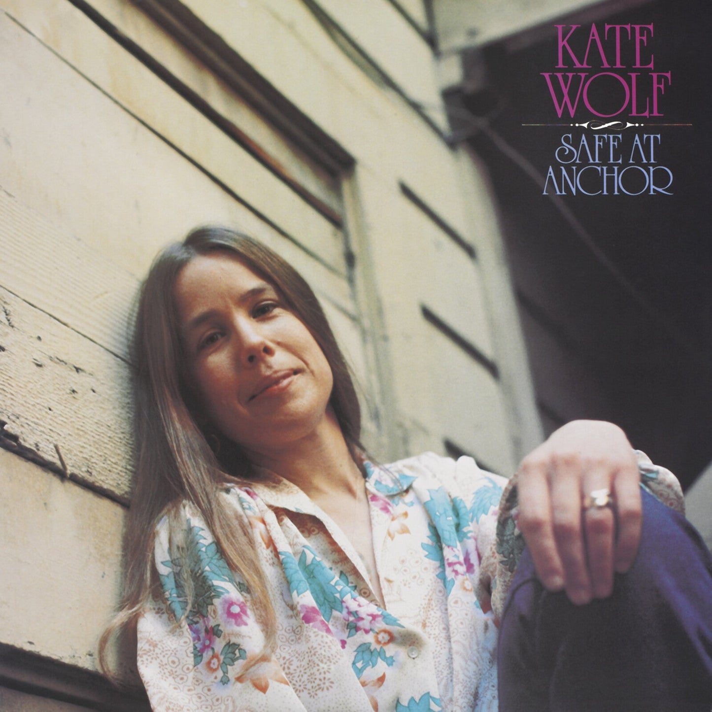 Kate Wolf leans against a wooden wall on the cover of Safe At Anchor.
