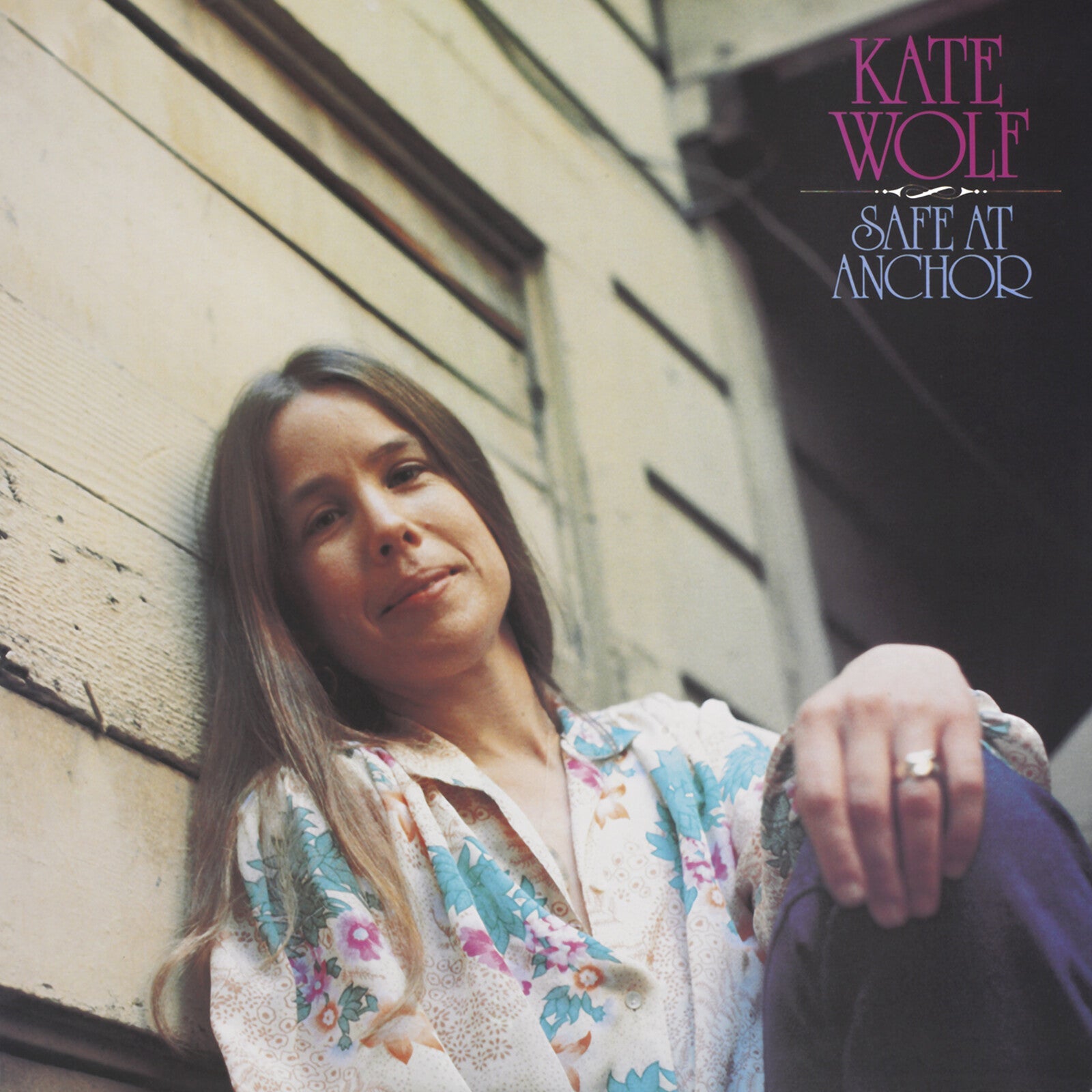 Kate Wolf leans against a wooden wall on the cover of Safe At Anchor.