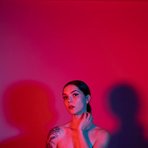 A woman with a tattoo poses against a vibrant red background with blue lighting.
