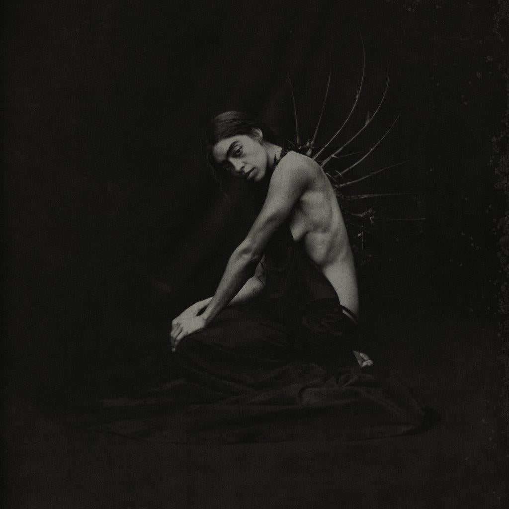 Black and white portrait of Kelsey Lu with feathered wings, kneeling.