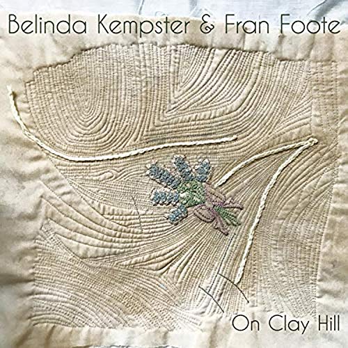 "Album cover with embroidered beige quilt featuring a blue flower design and artist names."