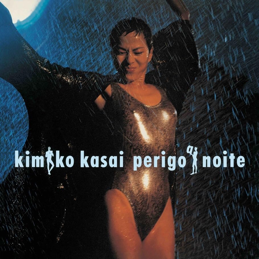 Woman in wet, shiny bodysuit stands in falling blue rain.