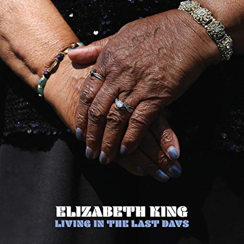 Close-up of hands wearing rings and bracelets over a dark textured garment.