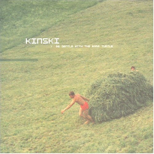 A shirtless man in red shorts pulls a large pile of hay across a hill.