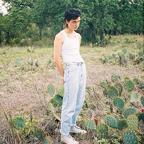 A person in a white tank top and jeans stands in a cactus field.