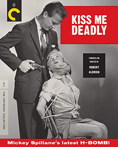 A man in a suit holds a gun over a woman tied to a chair.