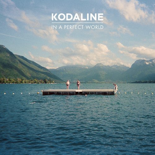 Three people stand on a wooden dock in a lake surrounded by mountains.