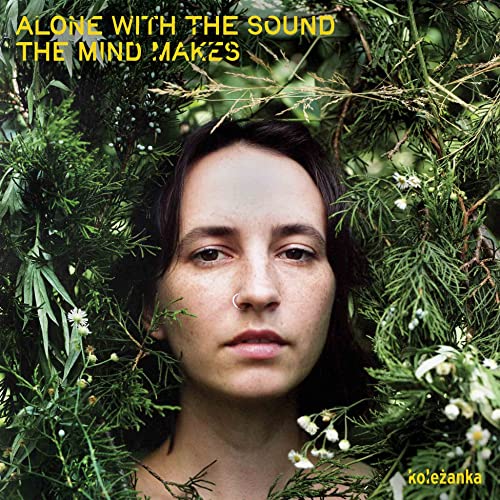 A person with dark hair and a nose ring framed by green foliage.