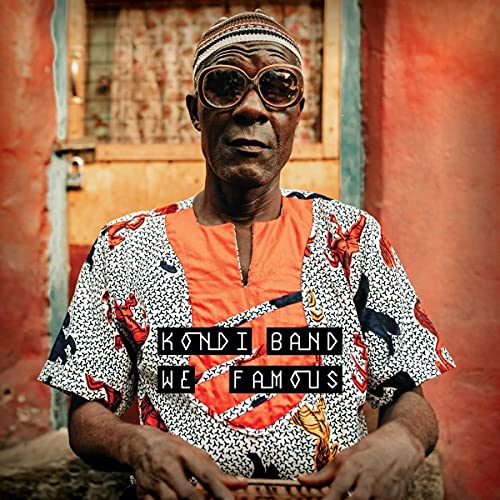 Older man with sunglasses and colorful shirt standing in front of a doorway.