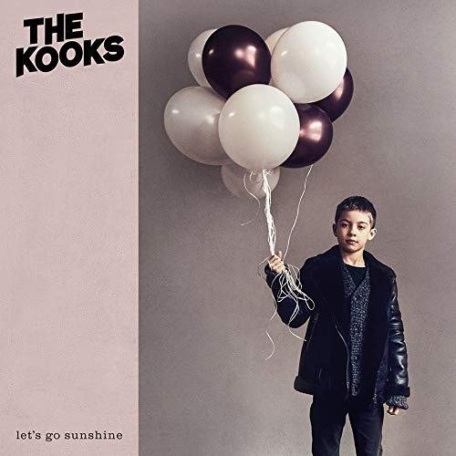 A young boy in a black jacket holds a bunch of white and dark balloons.