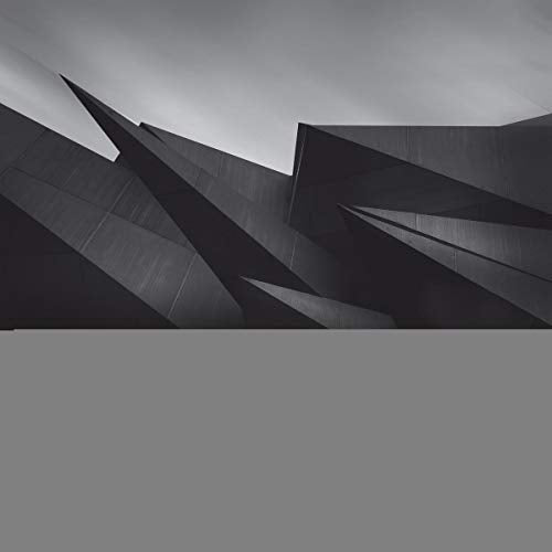 A black-and-white image of abstract, angular, dark gray shapes against a cloudy sky.