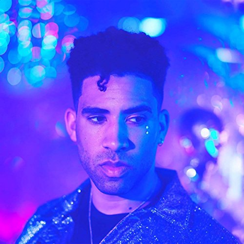 A man with dark hair and facial gems under blue and purple lighting.