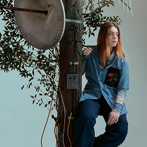 A woman with reddish hair sits by a utility pole with a satellite dish.