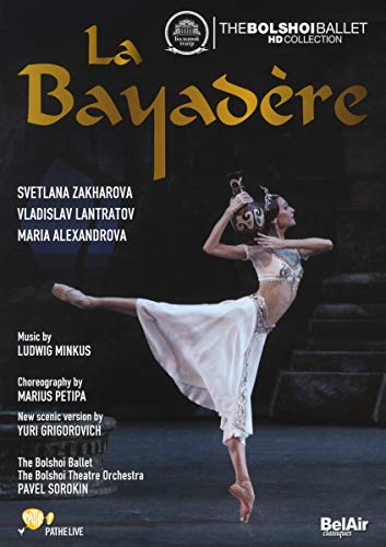 A ballerina in a white costume performs on stage, holding a vessel above her head.