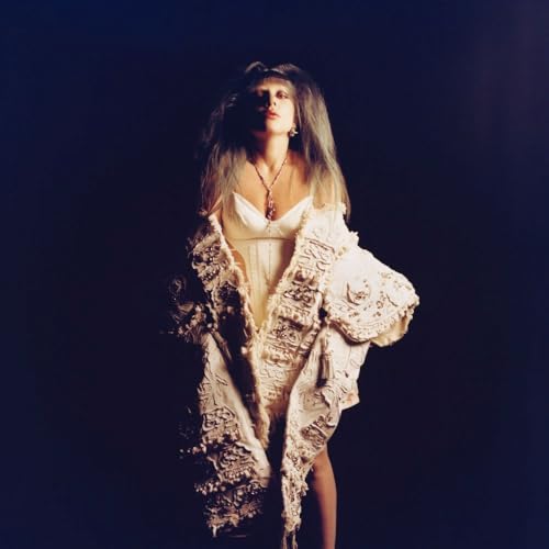 Lady Gaga in white dress and textured coat, looking upwards.