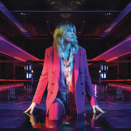 Woman kneeling in water, wearing pink blazer and shiny bodysuit, under neon-lit ceiling.