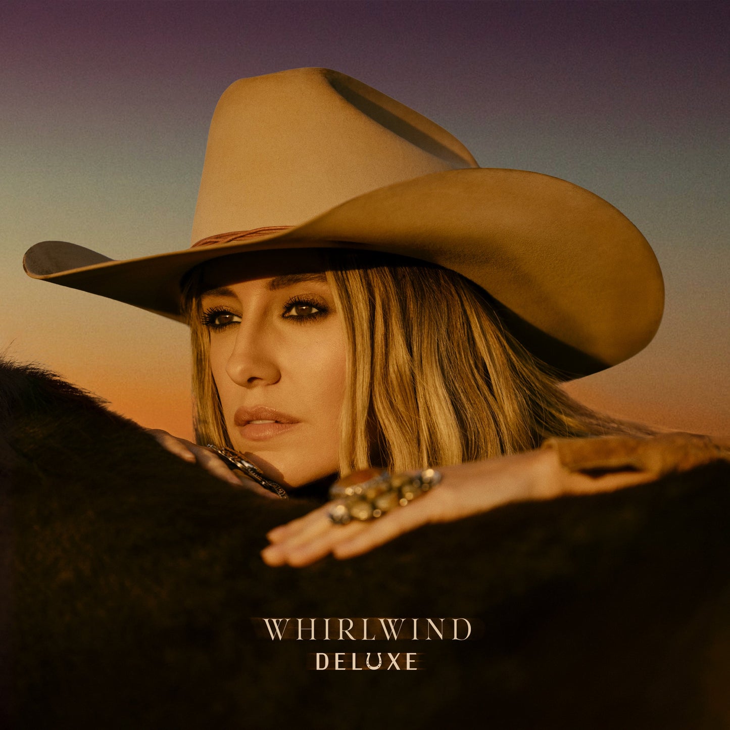 Lainey Wilson wearing a cowboy hat, leaning on a horse against a sunset background.
