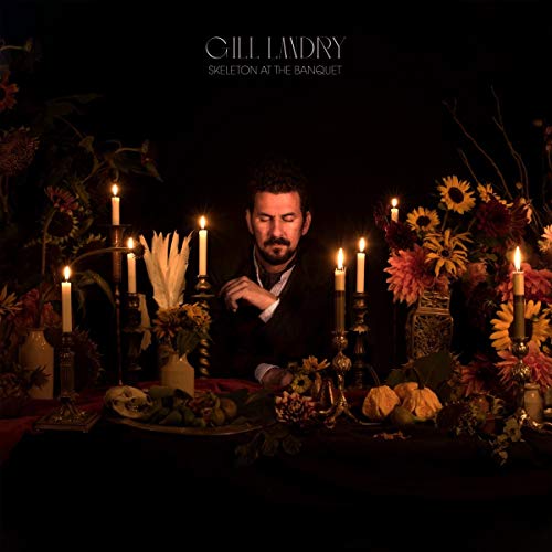 Man sits at a candlelit table with flowers and food, surrounded by darkness.