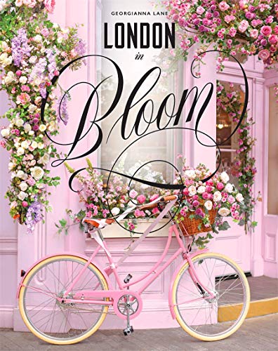 The image depicts a pink bicycle adorned with flowers, positioned in front of a doorway. The bicycle is facing to the right, with its front wheel slightly turned towards the viewer. The frame features the title "London in Bloom" prominently displayed. Key elements of the image include: * A pink bicycle * Flowers attached to the bicycle and surrounding the doorway * A doorway behind the bicycle A suitable alt text for this image could be: "Pink bicycle with flowers in front of a
