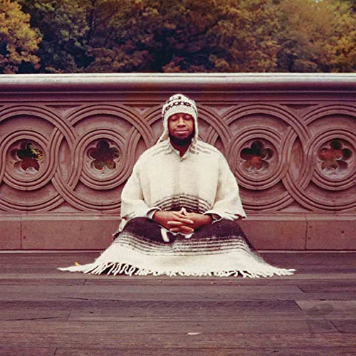 Laraaji seated in meditation, wearing white and striped garments.