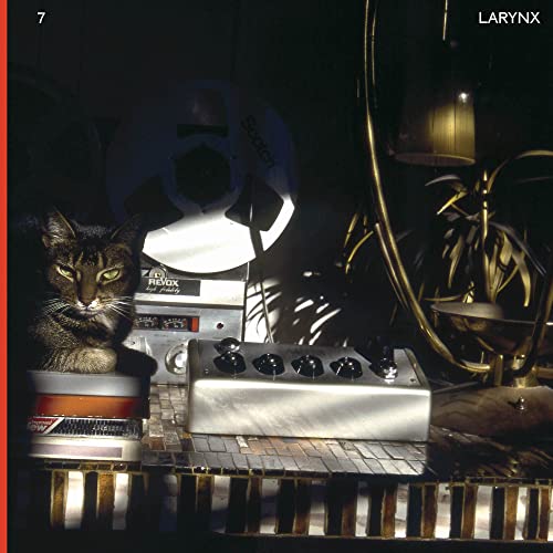 A cat sits on a stack of tapes next to audio equipment and lamps.