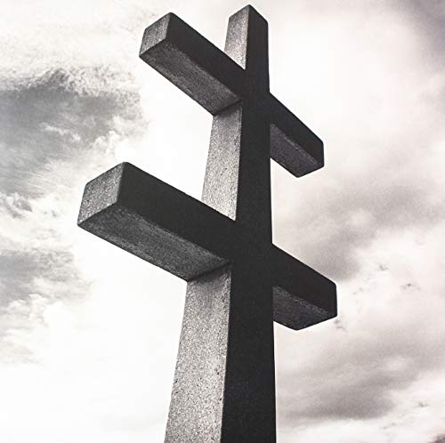 Black and white image of a tall, stone Eastern Orthodox cross against clouds.