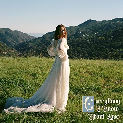Laufey in a white dress standing in a grassy field with mountains.