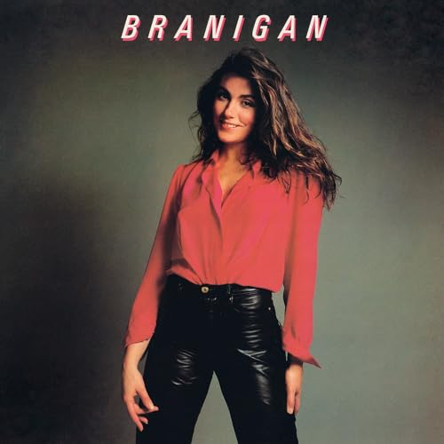 Laura Branigan wearing a red blouse and black leather pants against a grey background.