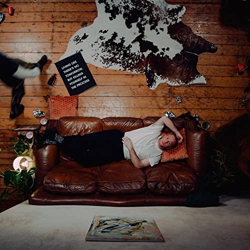 A man lies on a leather sofa with a sign and cowhide rug nearby.