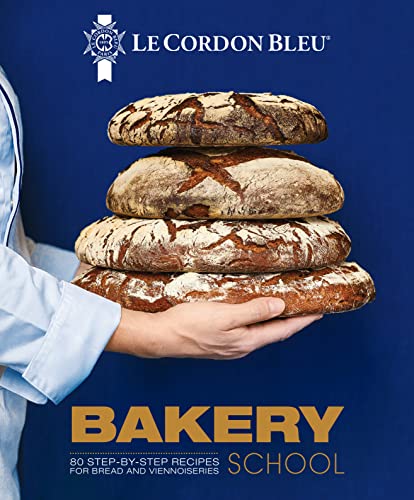 A chef holds a stack of four rustic loaves of bread against a blue background.