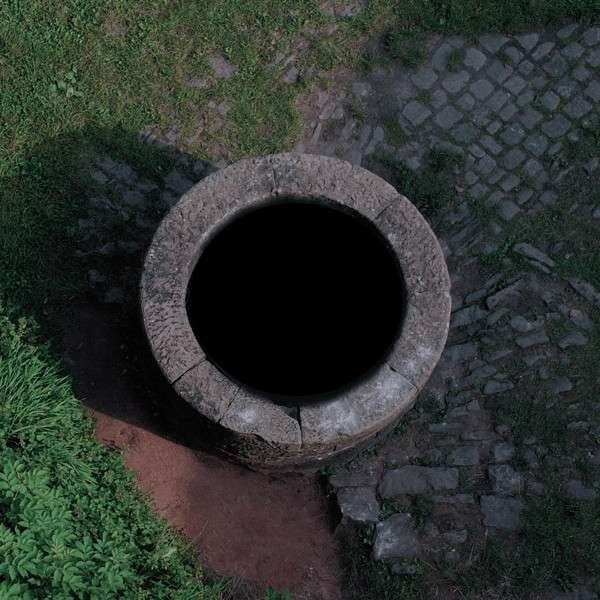 Overhead view of a stone well surrounded by grass and brick.