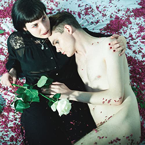 A woman in a black dress and a shirtless man lying among rose petals.
