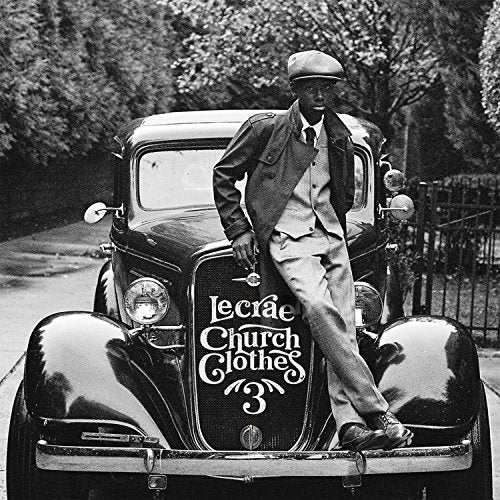 Black and white photo of Lecrae posing on a vintage car hood.