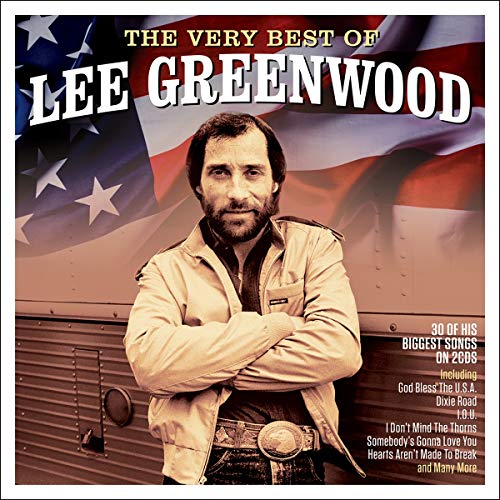 Lee Greenwood with arms crossed in front of an American flag background.