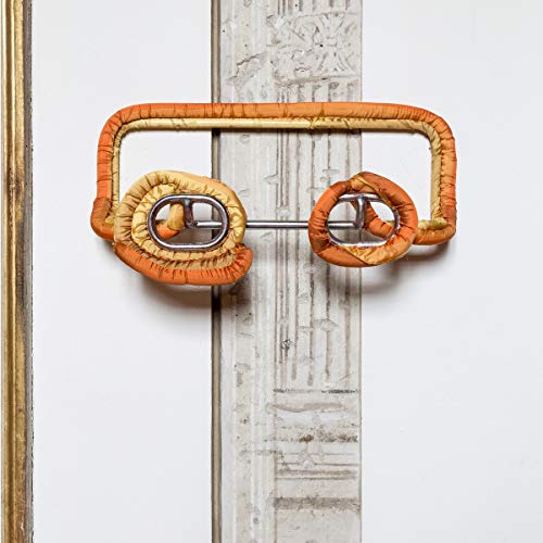 Abstract orange and yellow sculpture resembling eyeglasses against a wall.