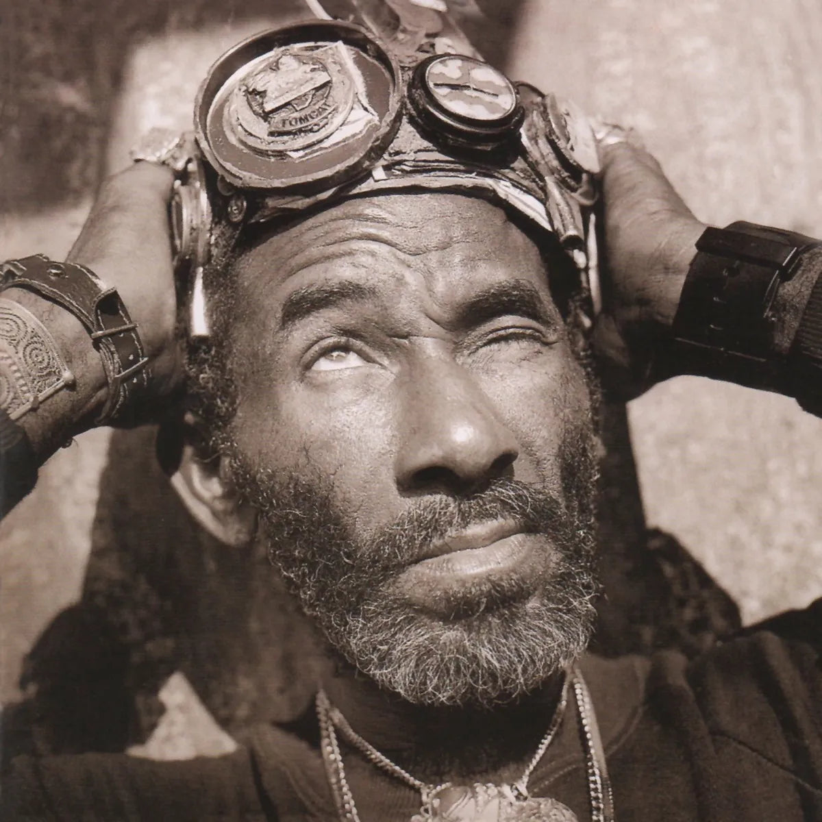 Sepia-toned portrait of a man wearing goggles on his forehead, looking upward.