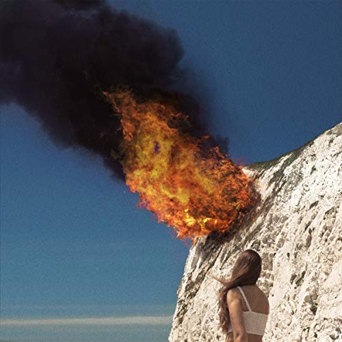 Woman looking at flames erupting from a white cliff under a blue sky.
